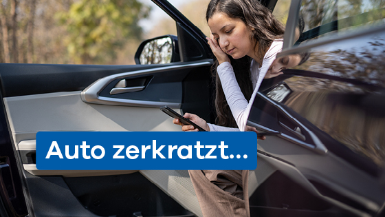 Junge Frau sitzt im Türbereich des Autos und schaut auf ihr Handy. 