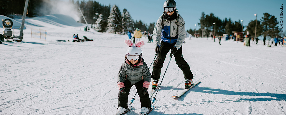 Elternteil und Kind fahren Ski gemeinsam auf der Piste