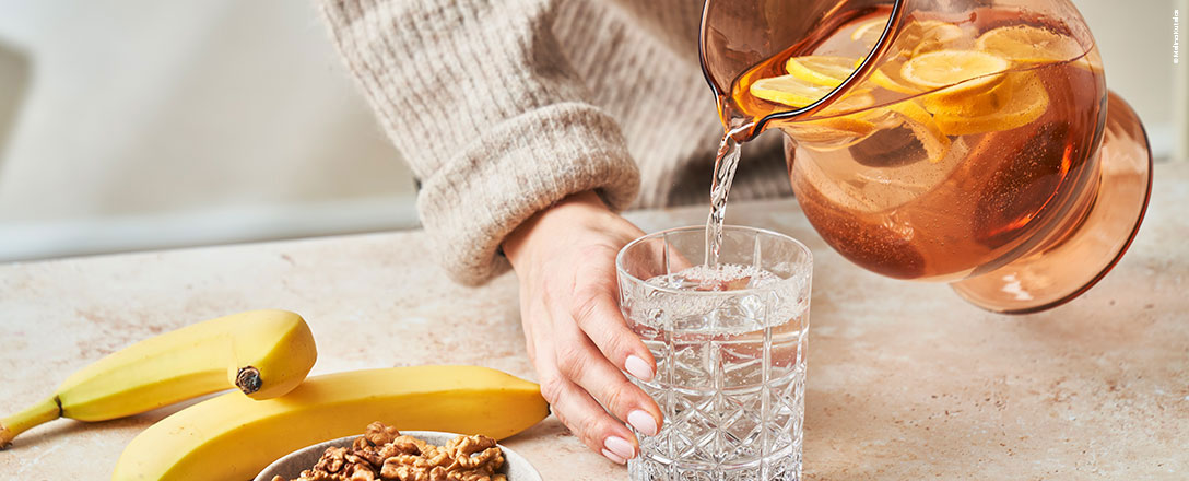 Frau gießt Zitronenwasser in ein Wasserglas