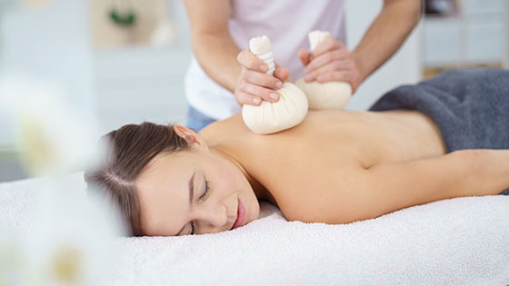 Frau lässt sich mit Kräuterstempel massieren