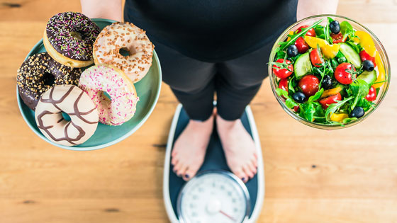 Person steht auf Waage und hält zwei Schalen in den Händen
