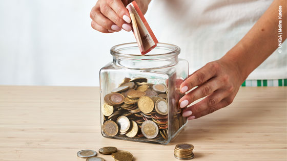 Geldschein wird in Spardose geworfen