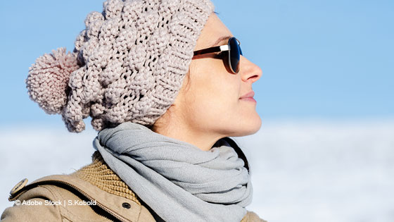 Frau mit Mütze und Sonnenbrille sieht in die Luft 