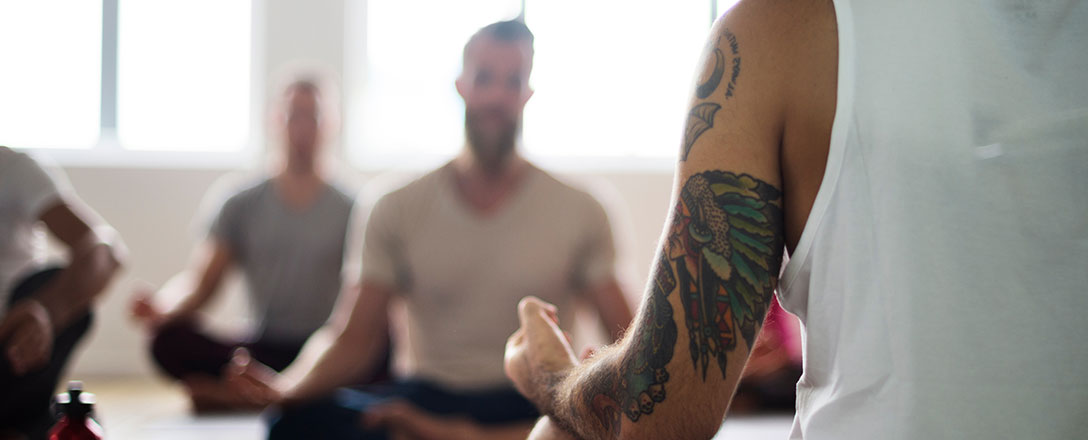 Männer sitzen im Schneidersitz beim Yoga-Unterricht
