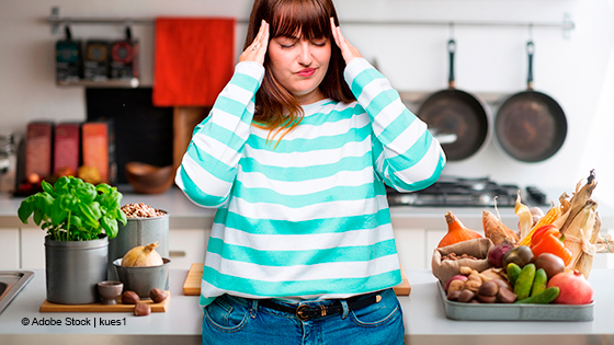 Frau steht in der Küche und greift sich am Kopf 