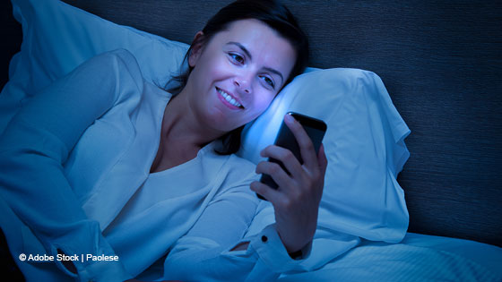Frau liegt im Bett und sieht auf ihr Handy, welches sie anleuchtet