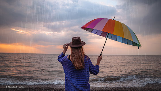 Frau mit Regenschirm schaut bei Regen aufs Meer