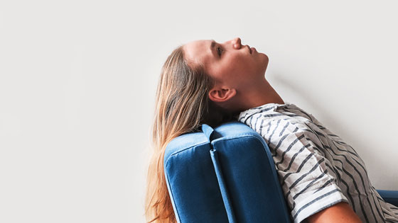 Frau sitzt auf einem blauen Stuhl und blickt an die Decke