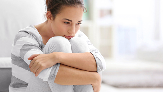 Frau sitzt am Boden und schlingt ihre Hände um die Knie