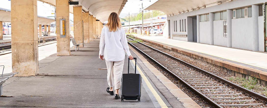 Person geht mit Rollkoffer Bahnsteig entlang