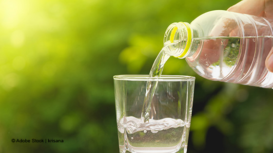 Hand hält Mineralwasser Flasche und gießt Wasser in ein Glas
