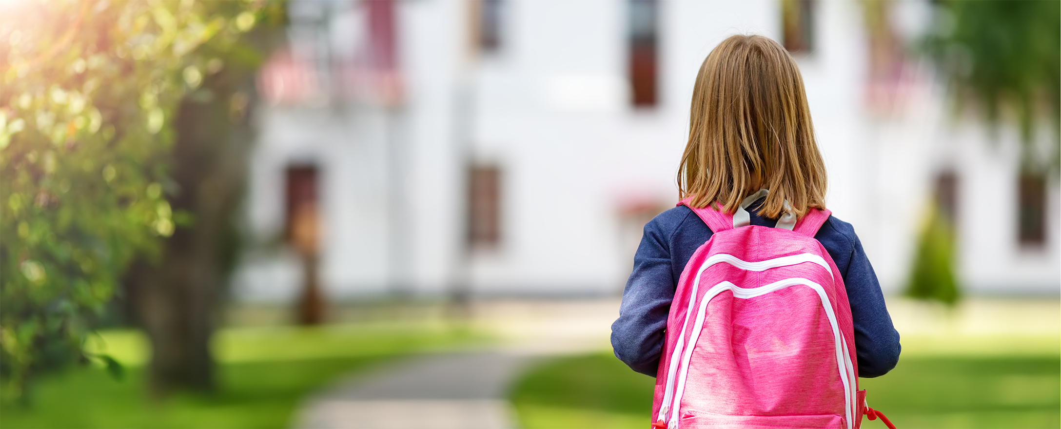 kind mit schultasche vor schule