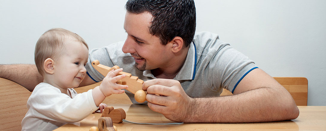 Vater spielt mit Kind am Tisch mit Holzspielzeug