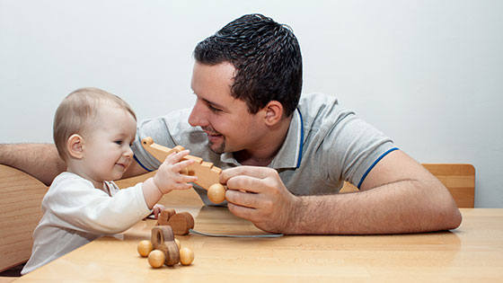 Vater spielt mit Kind am Tisch mit Holzspielzeug