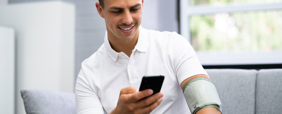 Junger Mann am Handy mit Blutdruckmanschette