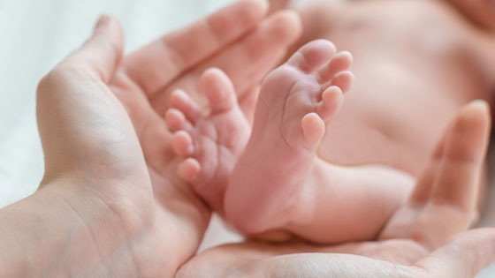 Hände sind schützend um die Füße eines Neugeborenen gefaltet