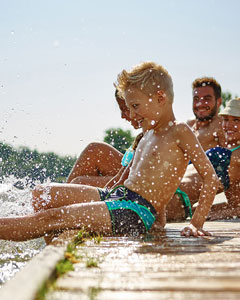 Kinder sitzen am Bootssteg und plantschen mit den Füßen im Wasser