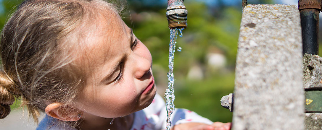 Mädchen trinkt Wasser aus Brunnenhahn
