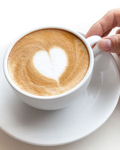 Hand hält Kaffeetasse mit Schaum-Herz