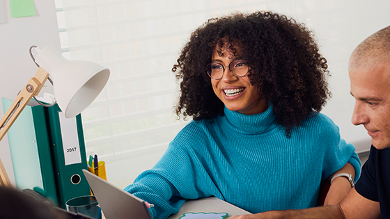 Junge Frau mit Locken und Pullover lächelnd beim Arbeiten