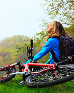 Frau sitzt in Wiese. Neben ihr liegt ihr Fahrrad.