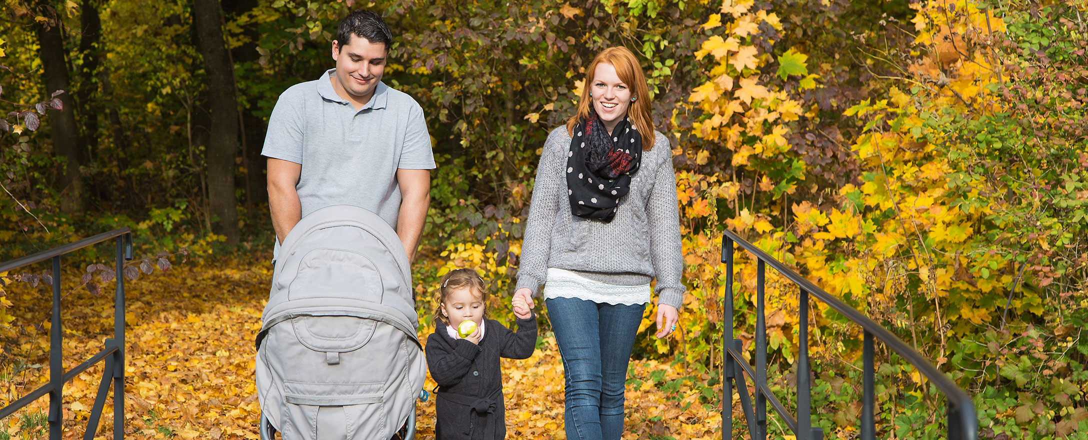 junge familie im herbst mit kinderwagen beim spaziergang