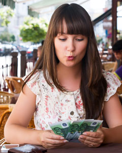 Frau sitzt in Cafe und hält Geldscheine in der Hand