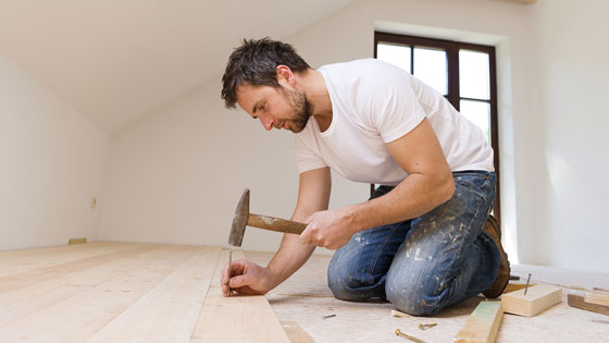 Mann schlägt Nagel in Holzboden