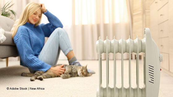 Frau sitzt mit Katze vor Heizkörper