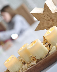 4 Kerzen stehen auf einem geschmückten Holzteller